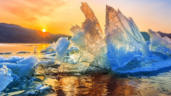 Imagen de un glaciar reditiéndose, con un sol muy brillante encima, representando la nueva era climática: la ebullición global.